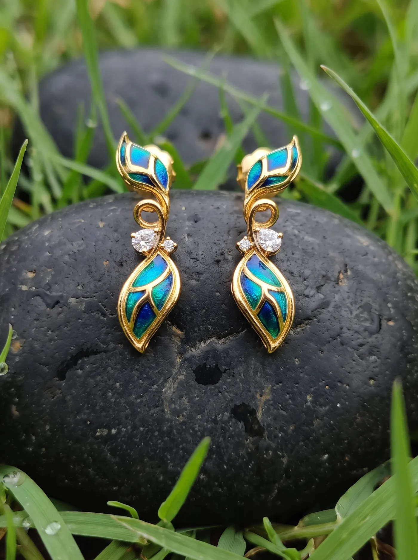 Contemporary earrings inspired by graceful foliage, adorned with peacock-toned cloisonné enamel and sparkling Swarovski crystals. Expertly crafted in 925 silver with gold plating, they bring together vibrant colour, fluid design, and timeless elegance.